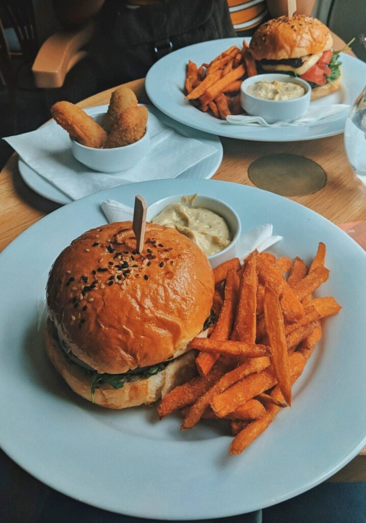 A white plate filled with a veggie burger and sweet potato fries on the side 