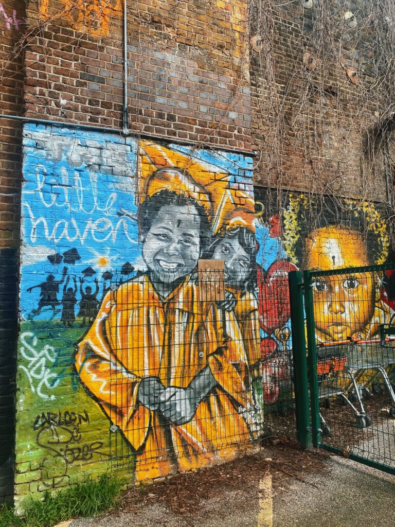 Mural on Castlehaven Road in Camden of 2 kids dressed in yellow and wearing graduation hats