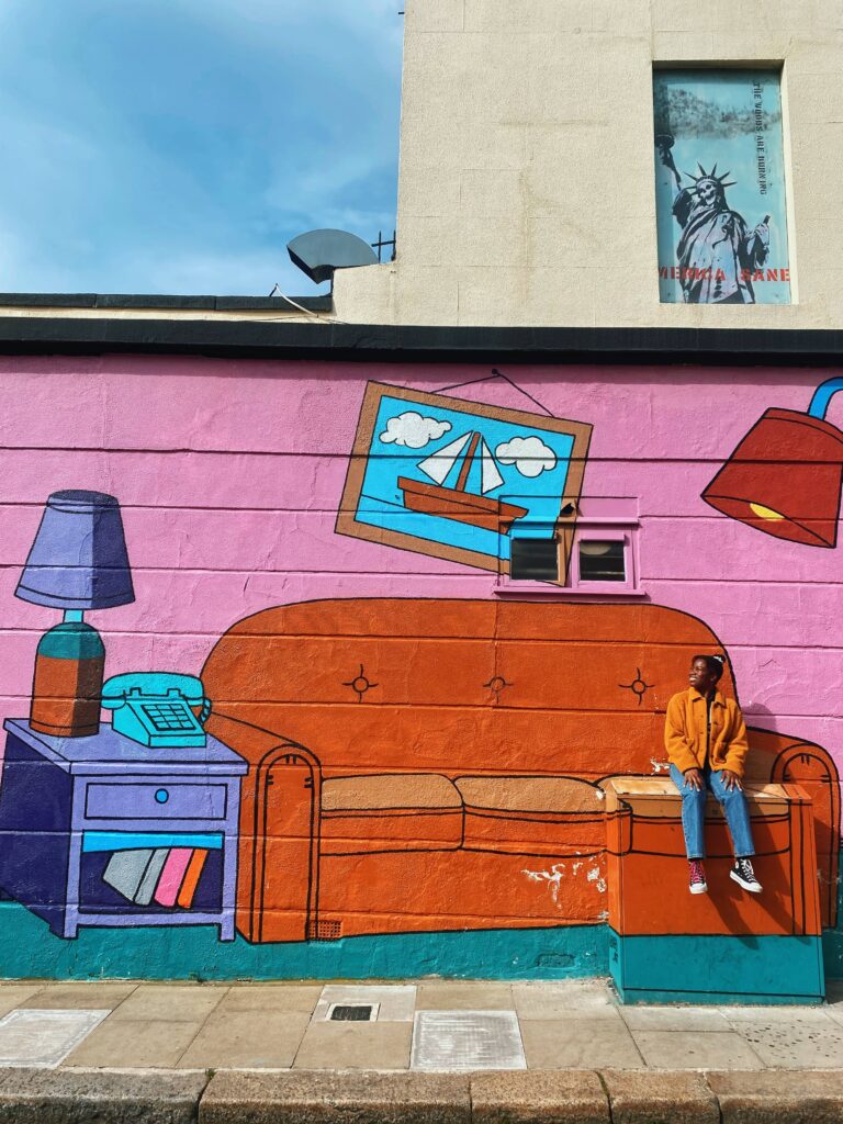 Abigail sitting on an electricity box that is part of the Simpsons coach mural in Camden