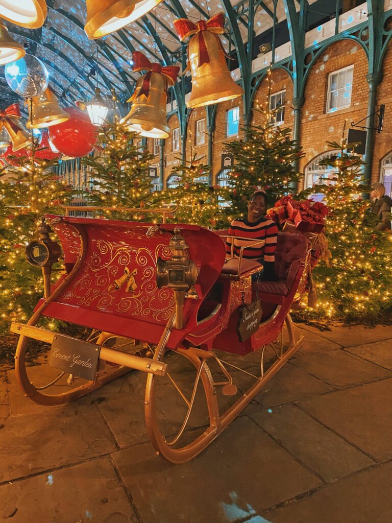 Abigail sitting on a red sleigh in Covent Garden, London
